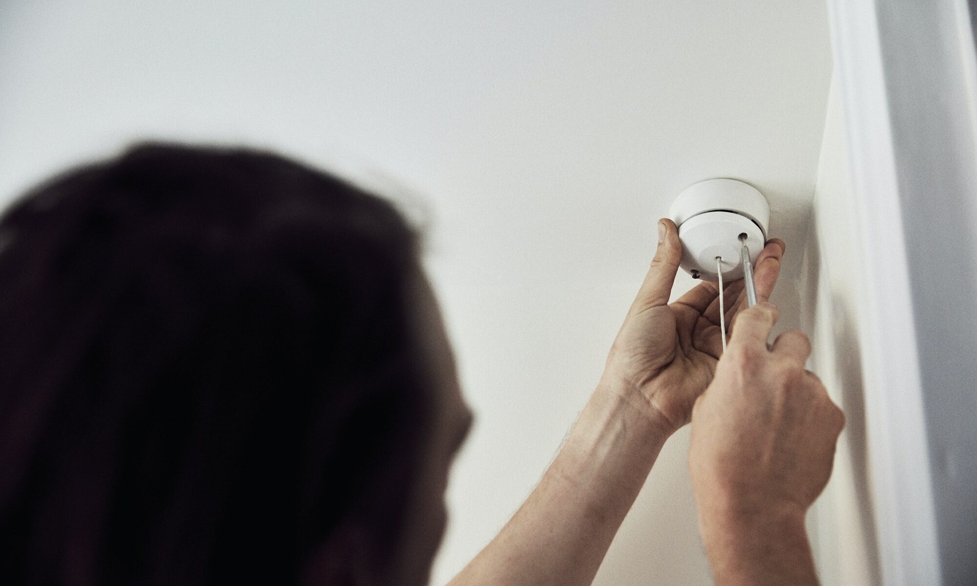 An electrician screwing the cap on a light fitting on the ceiling.