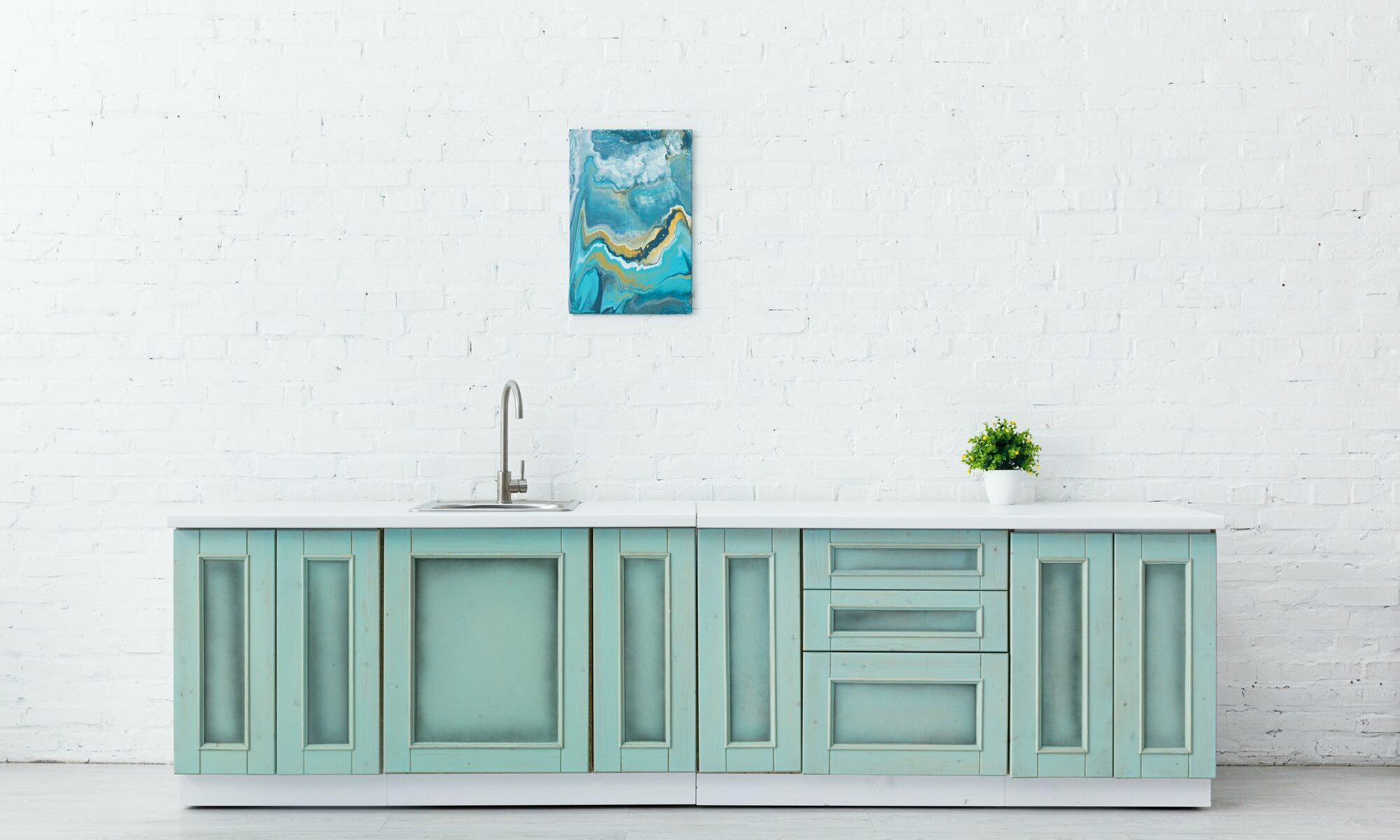 white and turquoise kitchen interior with sink, plant and abstract painting on brick wall