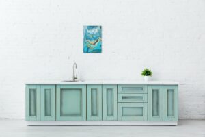 white and turquoise kitchen interior with sink, plant and abstract painting on brick wall