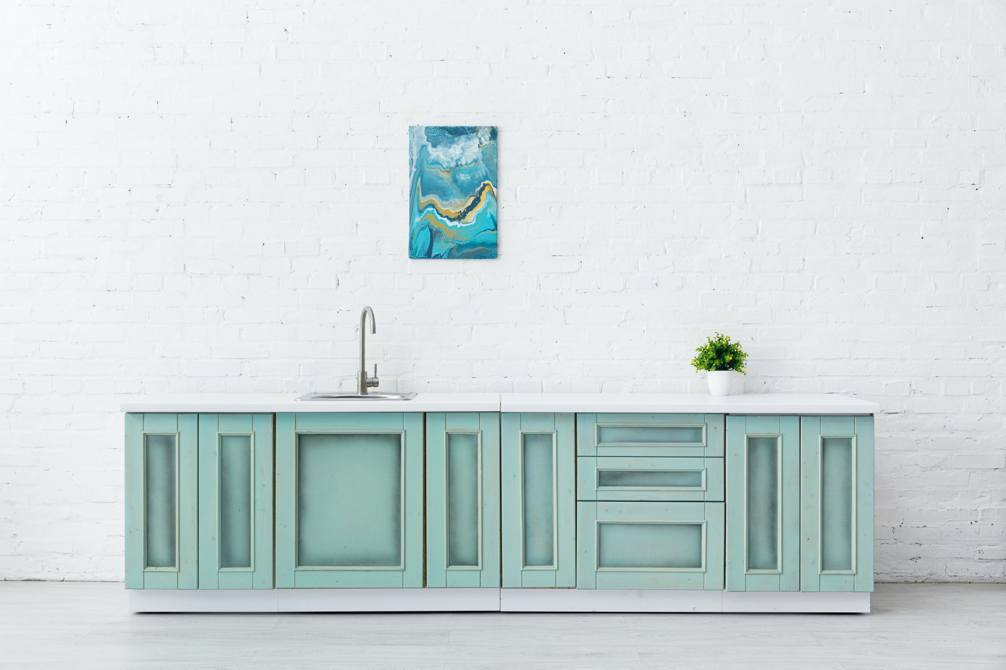 white and turquoise kitchen interior with sink, plant and abstract painting on brick wall