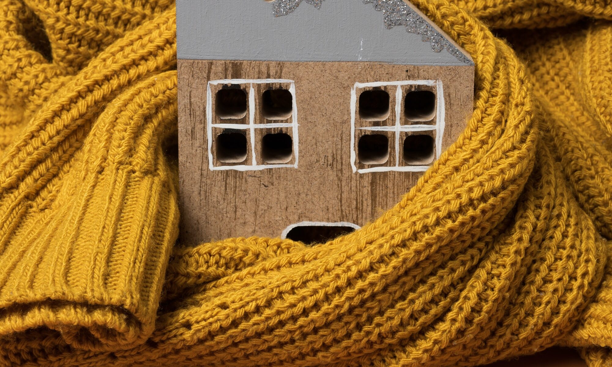 Wooden model of the house is wrapped in a warm knitted sweater. Loan concept for house insulation