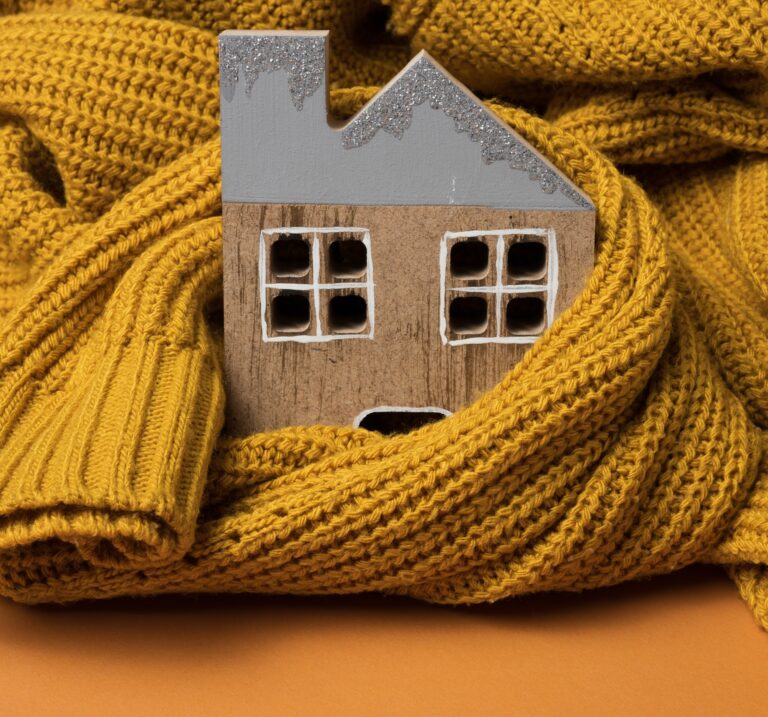 Wooden model of the house is wrapped in a warm knitted sweater. Loan concept for house insulation